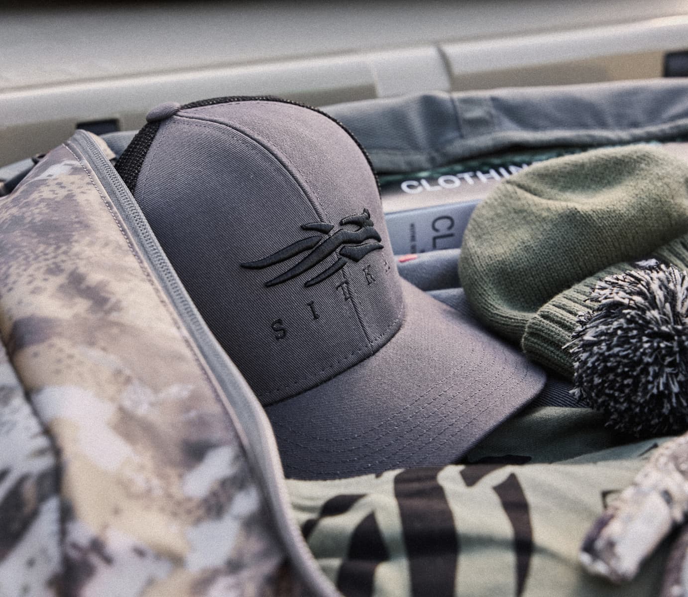 Assortment of Stocking Stuffers containing SITKA Tees, Hats, and Product Care in the Drifter Duffle 50L in Optifade Elevated | SITKA Gear Holiday Gift Guide