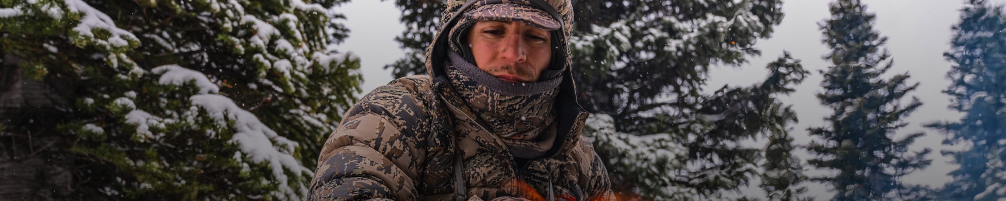 Adam Foss sitting by a camp fire in the HyperDown Jacket in Optifade Open Country | SITKA Gear Holiday Gift Guide