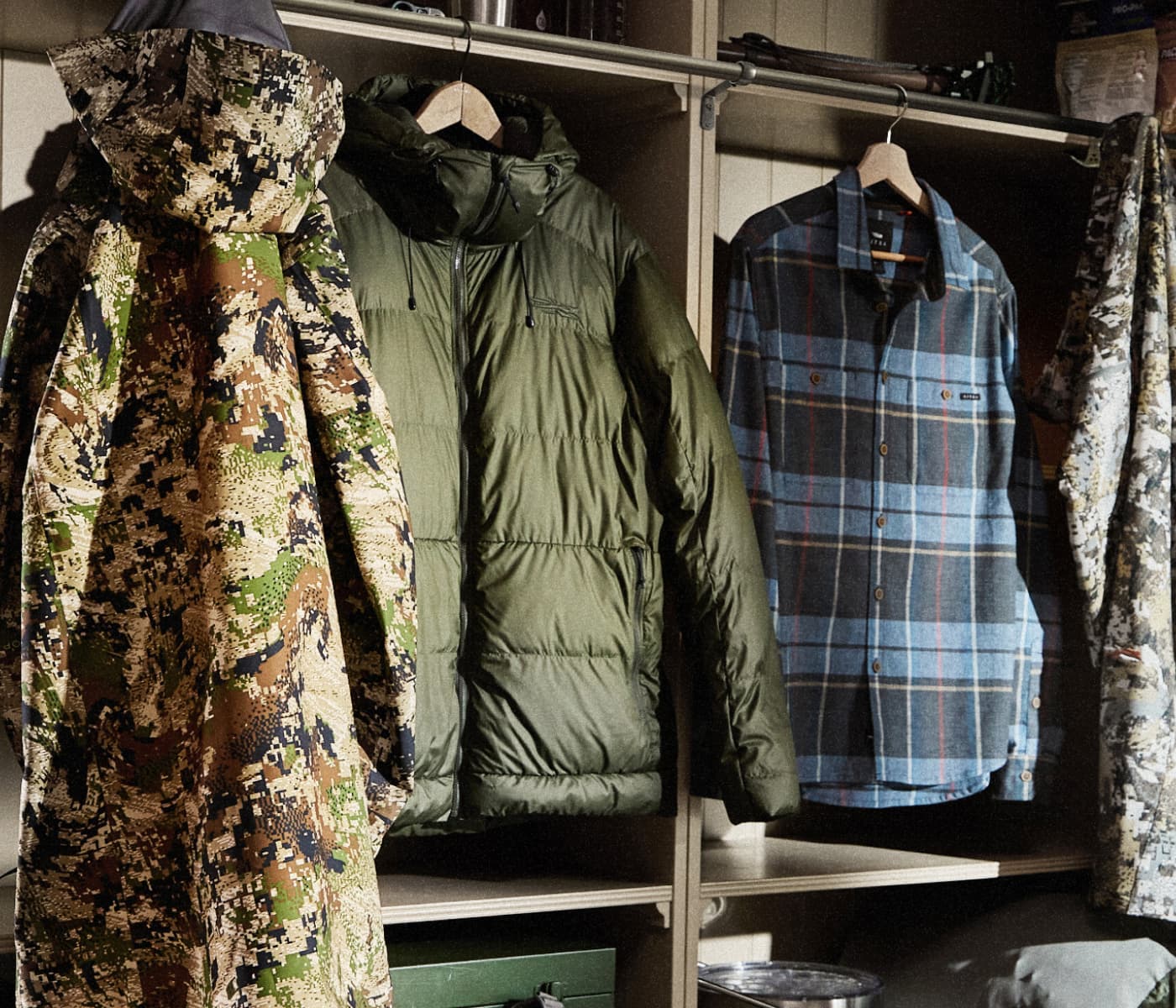 The Kodiak Jacket in Optifade Subalpine, HyperDown Jacket in Deep Lichen, and the Ambary LS Shirt in Pacific Fall Plaid hung in a mud room | SITKA Gear Holiday Gift Guide