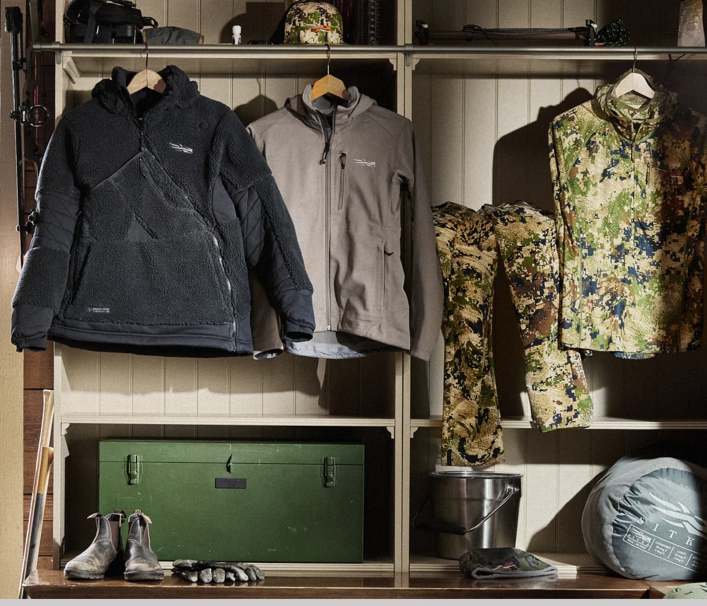 The Kodiak Jacket in Optifade Subalpine, HyperDown Jacket in Deep Lichen, and the Ambary LS Shirt in Pacific Fall Plaid hung in a mud room | SITKA Gear Holiday Gift Guide