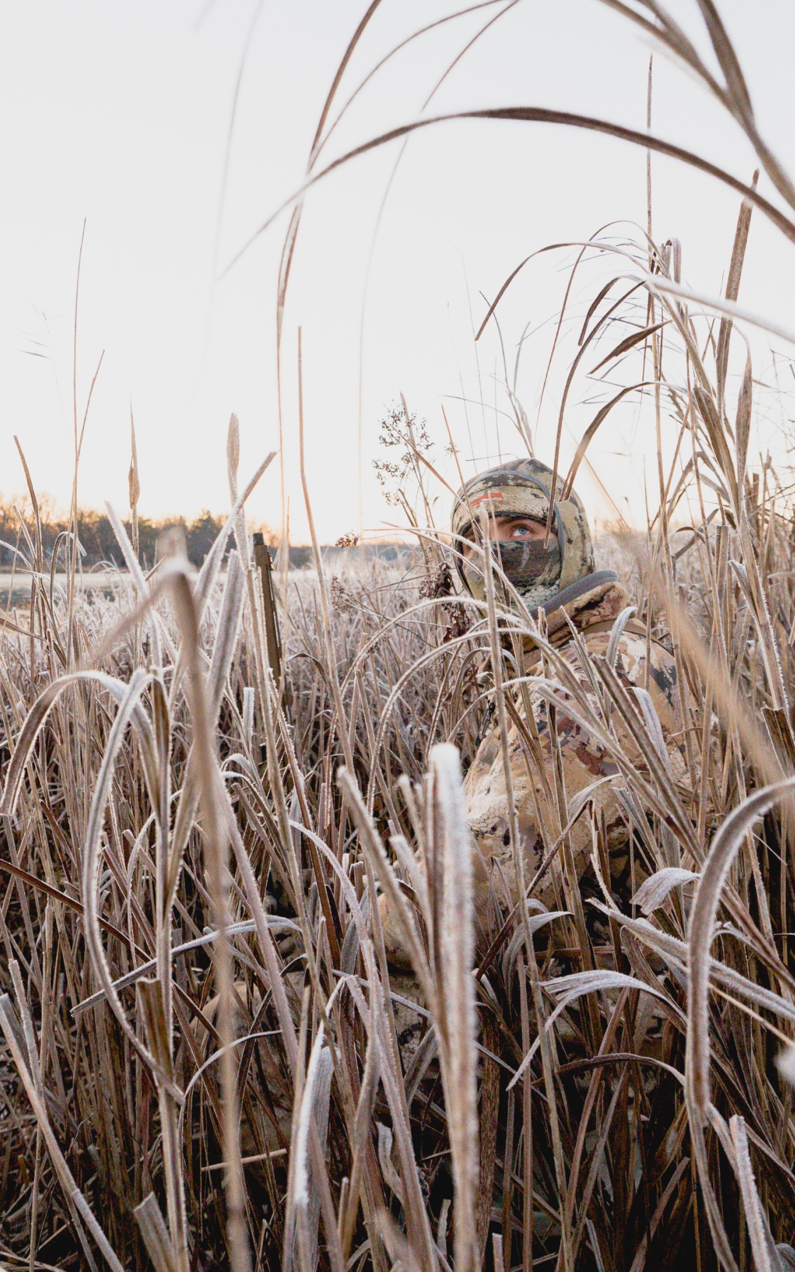 Man sitting in the tall grass watching the sky for waterfowl | SITKA Gear